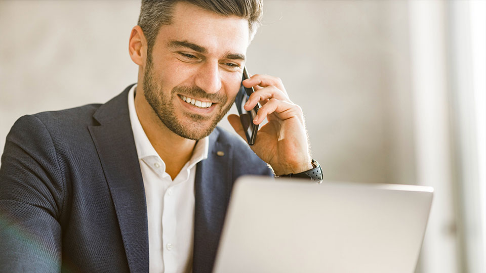 Mann sitzt am Computer und telefoniert