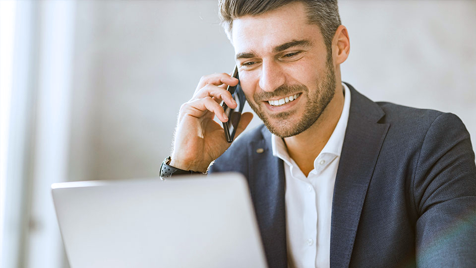 Business-Mann sitzt am Laptop und telefoniert