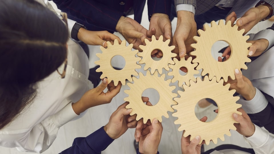 Several people hold wooden gears together, symbolizing a workflow process