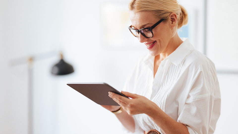 Frau mit Brille und in weißer Bluse bedient ein Tablet.