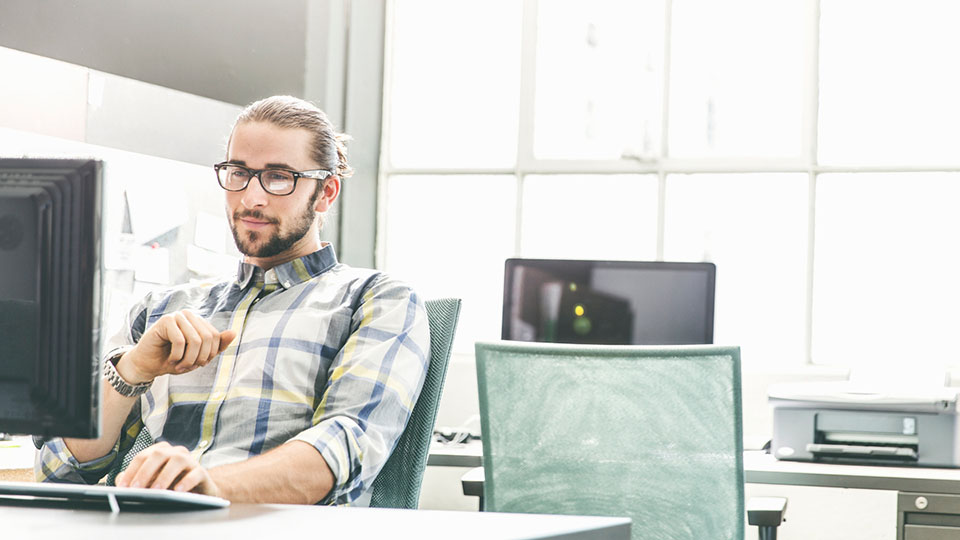 Technical writer with glasses and beard sits in front of a computer and creates technical documentation.