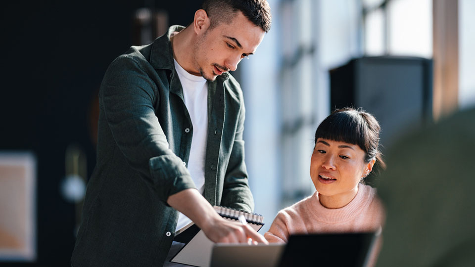 Two editors sit at a laptop and work together on a specialist article.