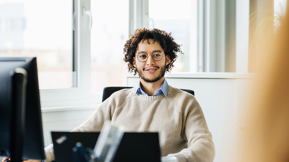 Mitarbeiter mit Brille und Locken arbeitet an einem Computer.