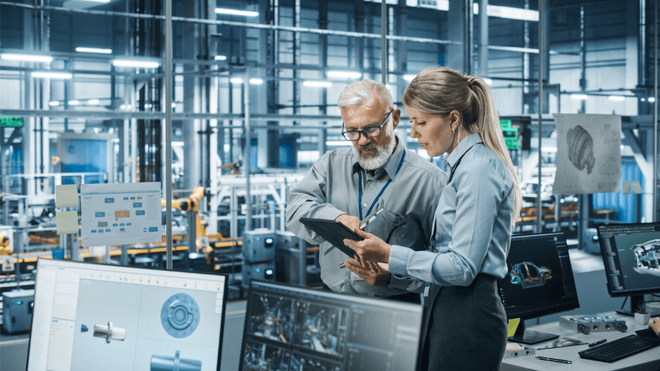 Zwei Personen stehen in einer industriellen Fabrikumgebung im Büro und schauen auf ein Tablet