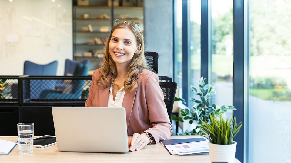 A woman sits at a desk and works on a laptop.