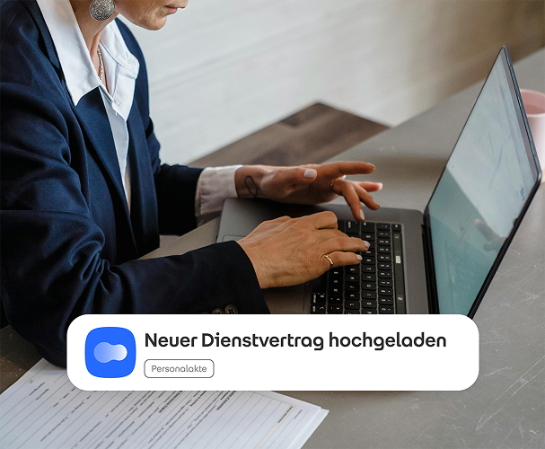 Foto einer Person, die am Laptop arbeitet. Im Vordergrund ist eine Benachrichtigung, dass ein neuer Dienstvertrag hochgeladen wurde.